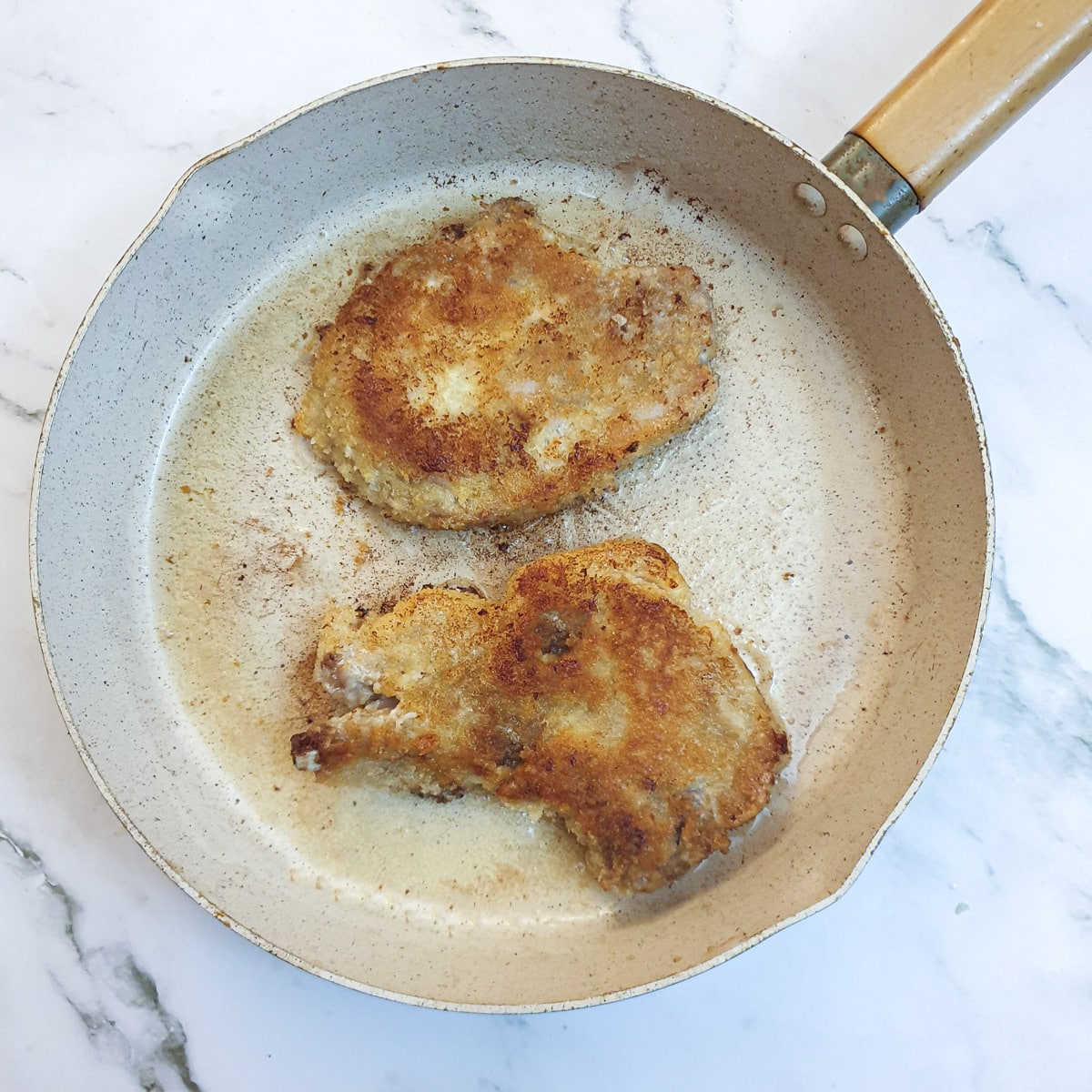 Two crumbed pork chops in a frying pan.