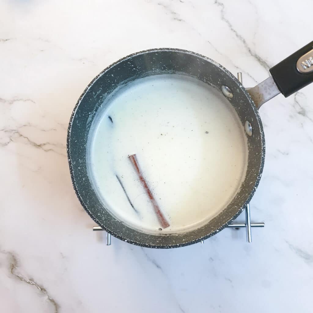 Milk with a cinnamon stick and vanilla pot heating in a saucepan.
