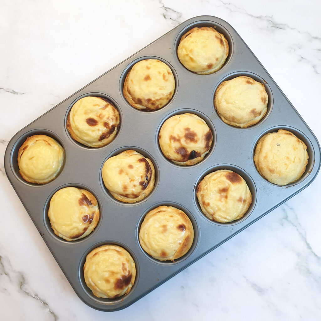 A 12-hole muffin pan containing 12 baked Portuguese custard tarts.