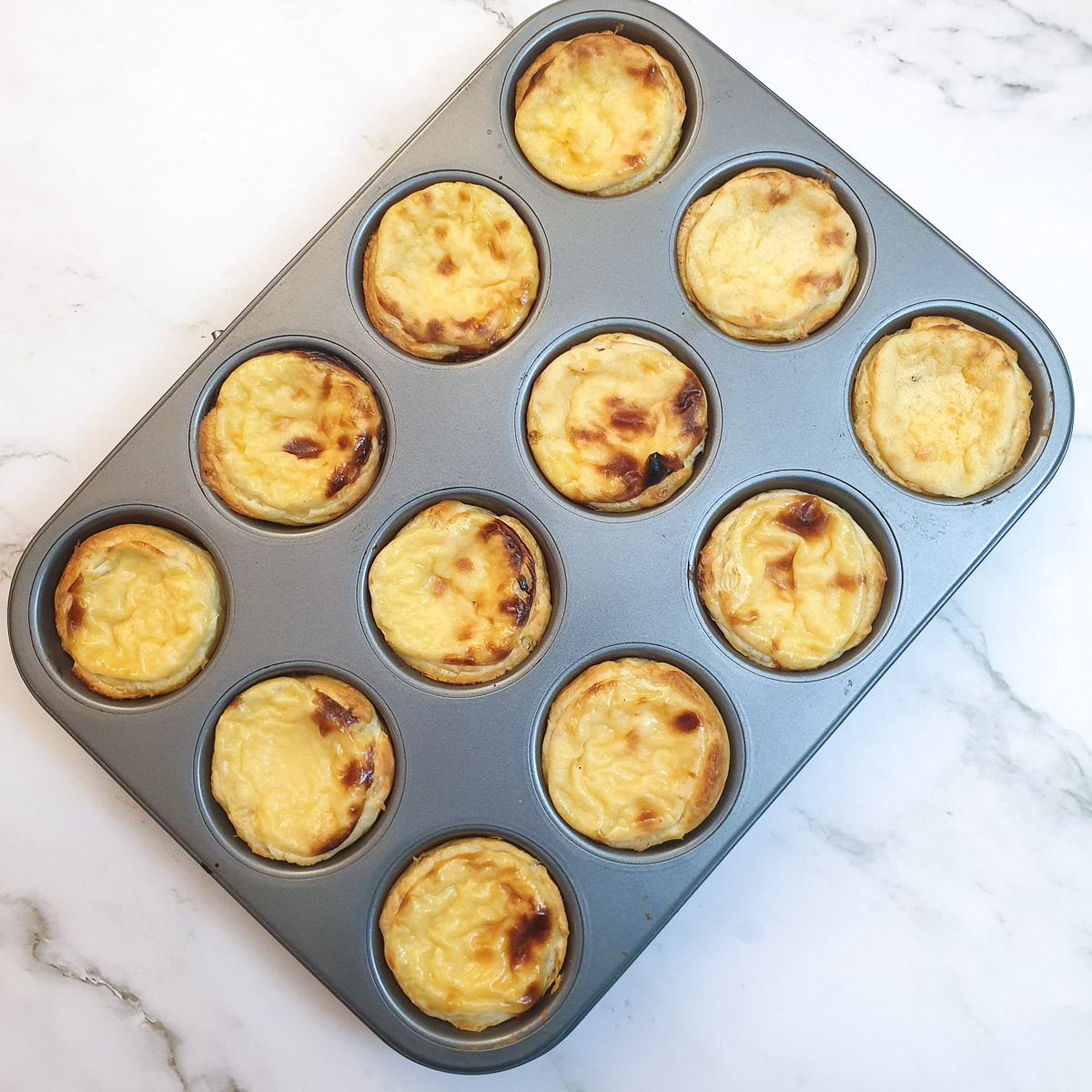 A tray of Portuguese custard tarts that have cooled, showing how the custard sinks down.