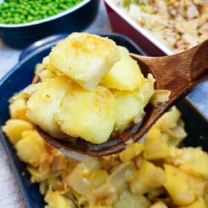 A closeup of a spoonful of saute potatoes and onions held over the serving dish.