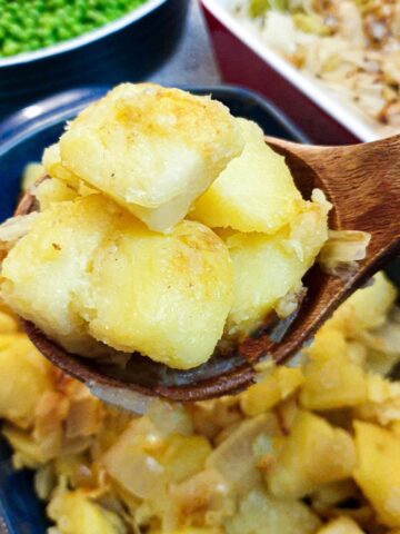 A closeup of a spoonful of saute potatoes and onions held over the serving dish.