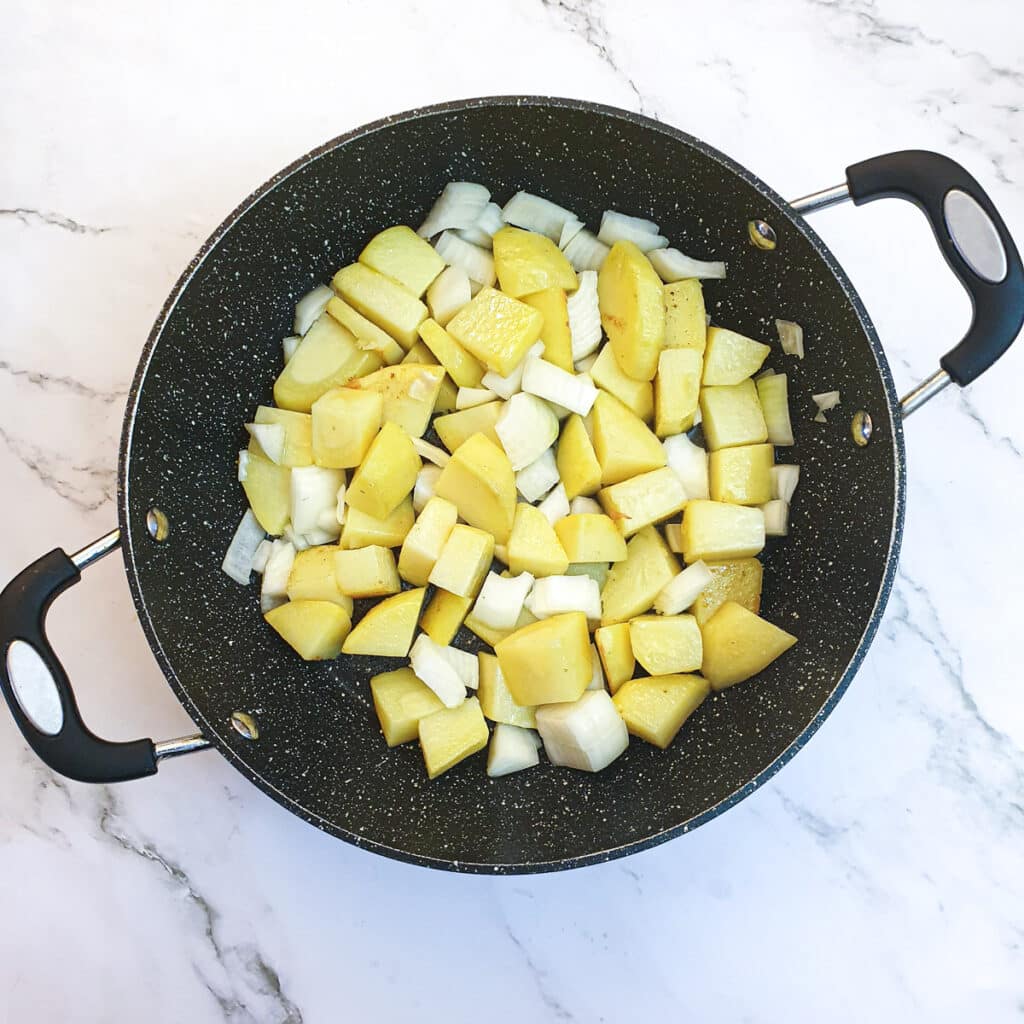 Chopped onions and potatoes in a frying pan.