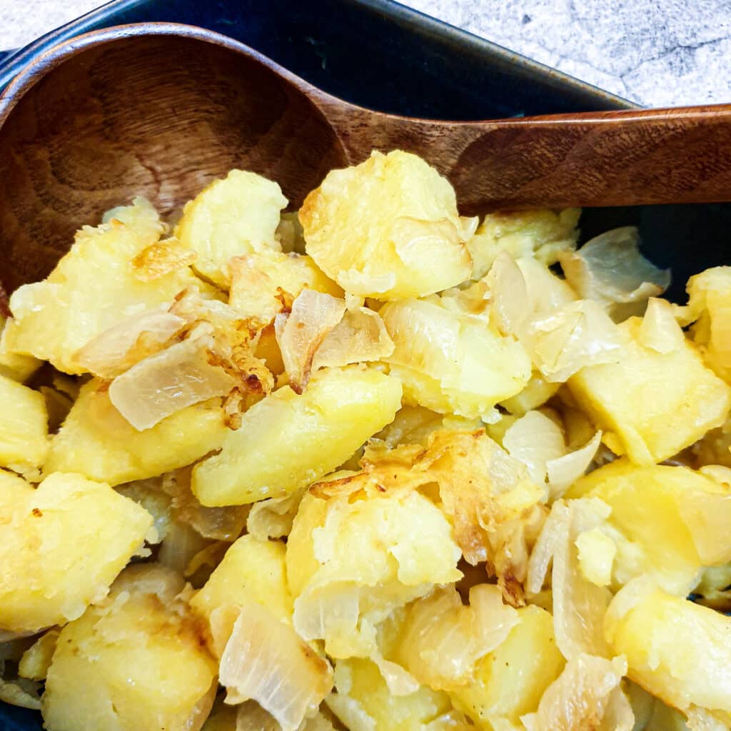 Closeup of saute potatoes with a brown wooden spoon.