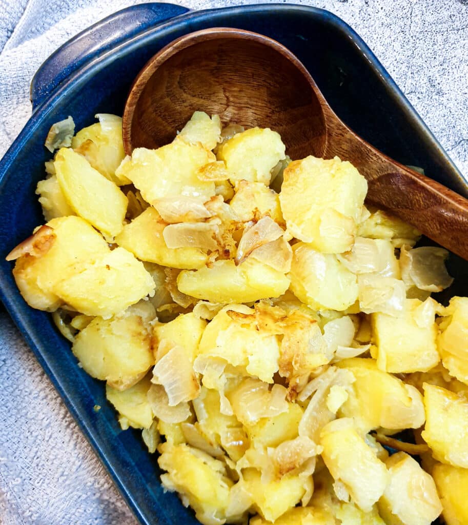 Saute potatoes and onions in a blue dish with a large wooden serving spoon.