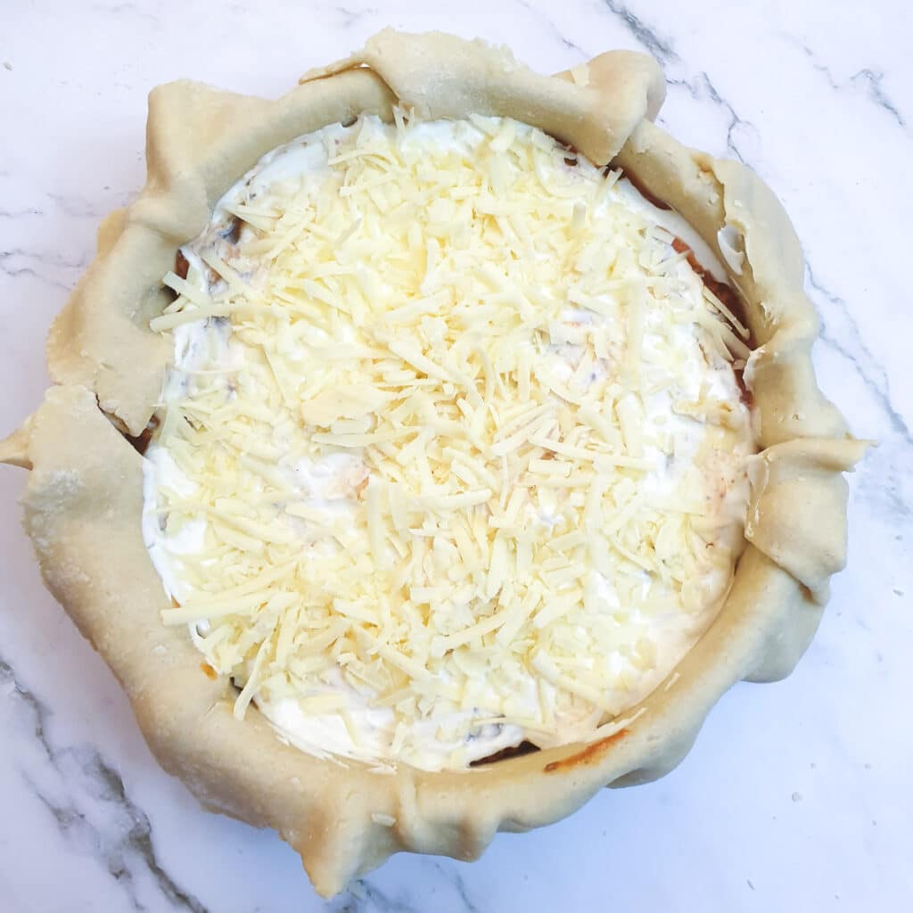 Sour cream and grated cheese on top of the meat filling in a pie dish.