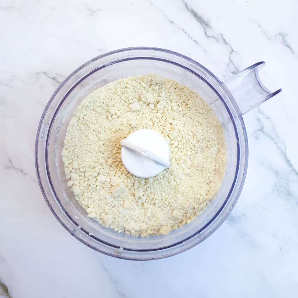 Flour, cheese and butter in a food processor after having been pulsed to a breadcrumb consistency.