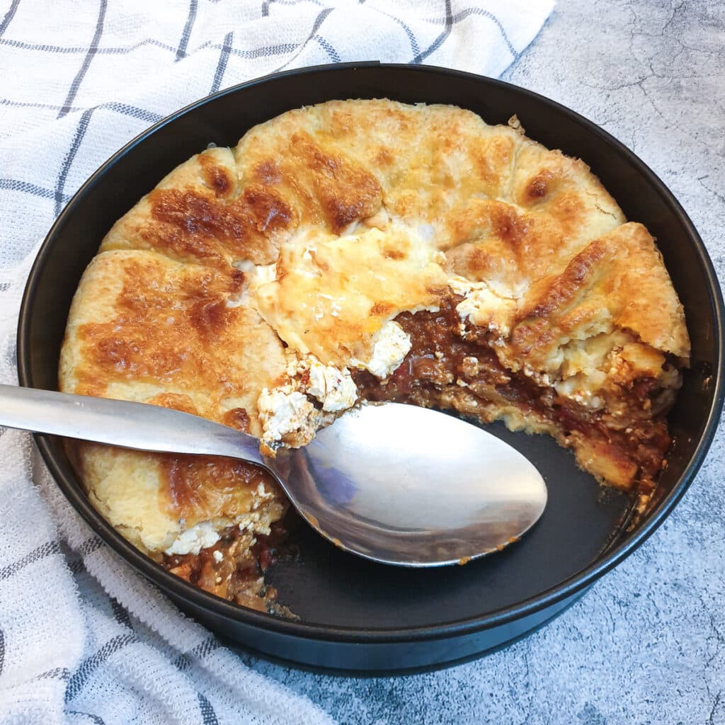 A tex mex beef pie in a baking dish with a slice removed to show the inside.