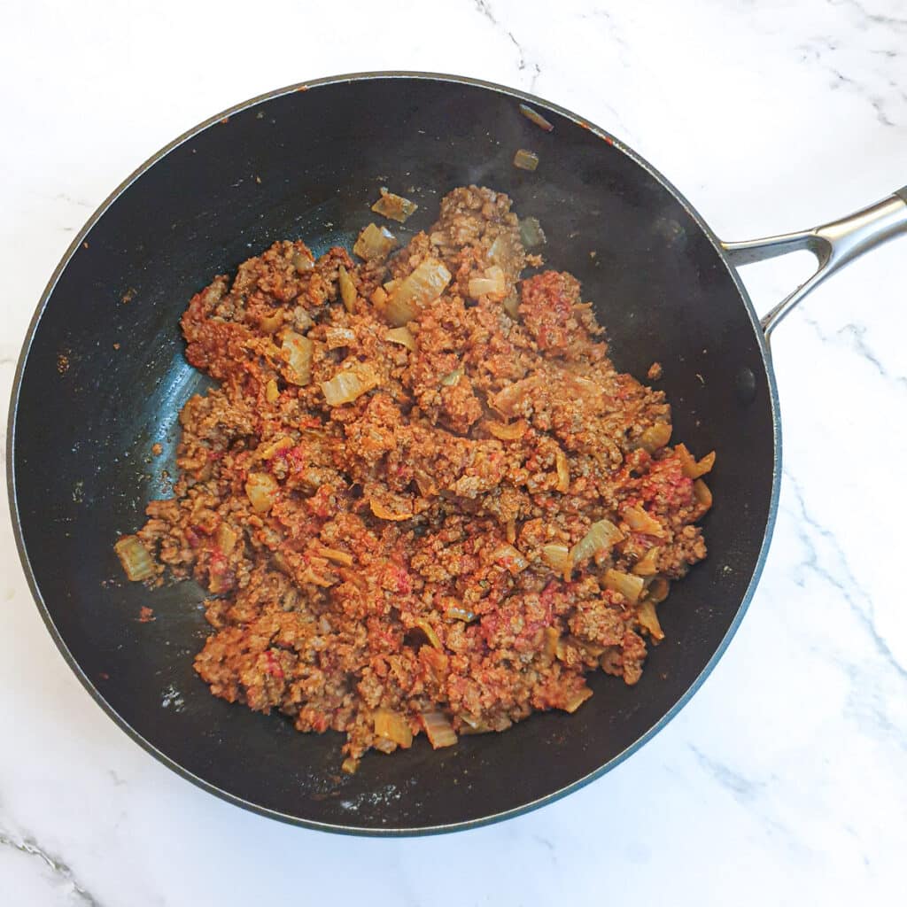 Ground beef in a pan after having been mixed with tomato paste, flour and fajita spices.