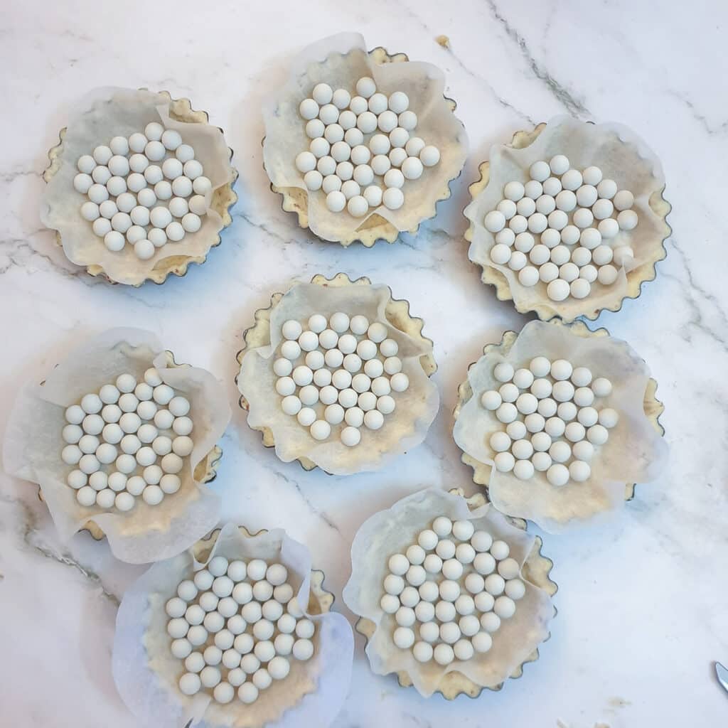 8 unbaked pastry shells lined with baking parchment and baking beans.