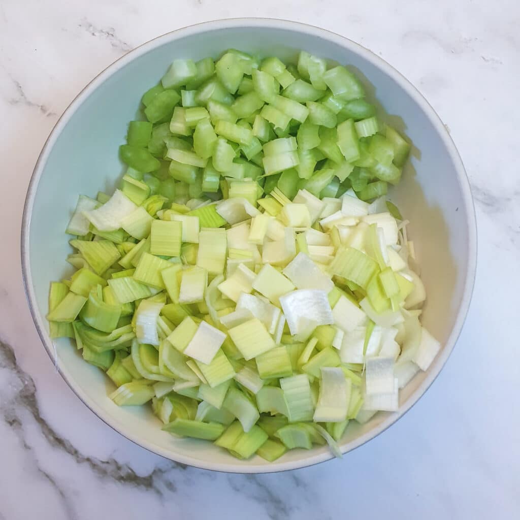 A white dish containing finely chopped leeks and celelry.