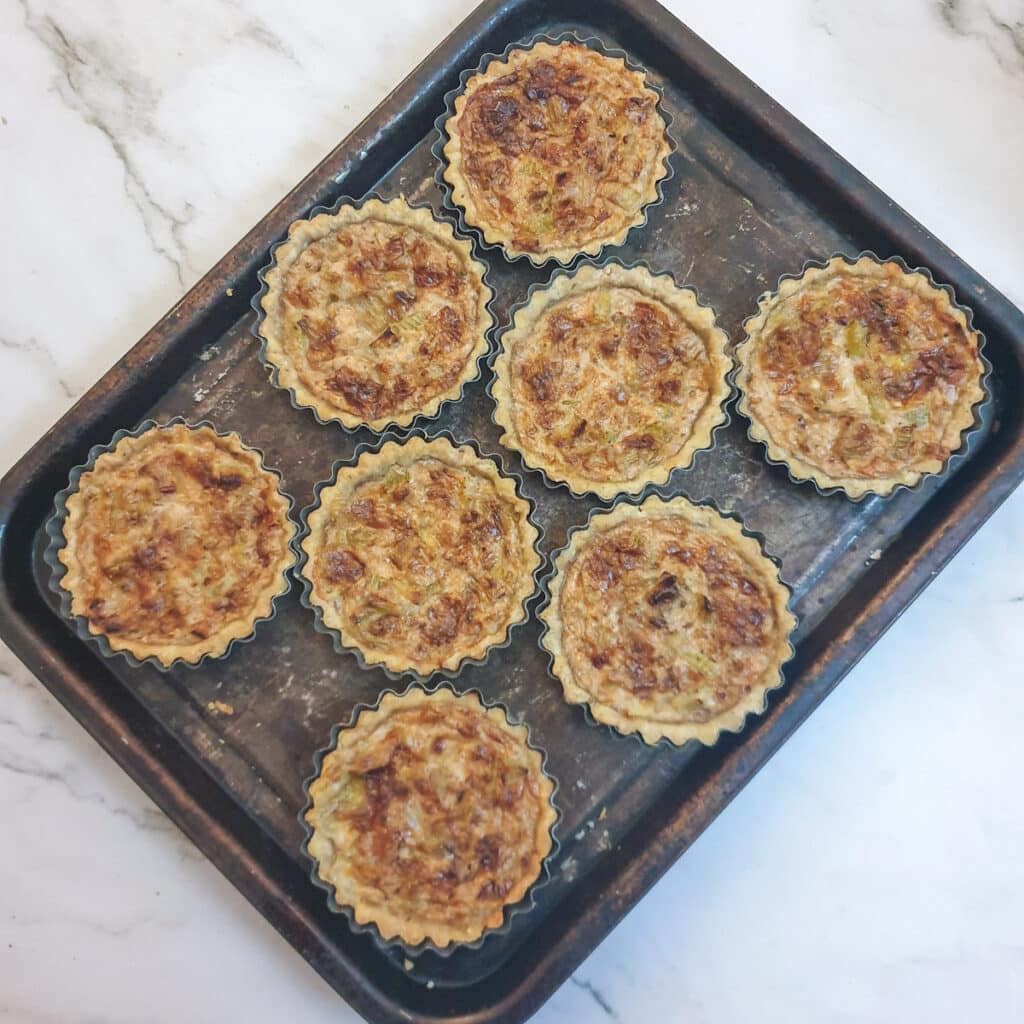 8 baked stilton and walnut tarts on a baking tray.