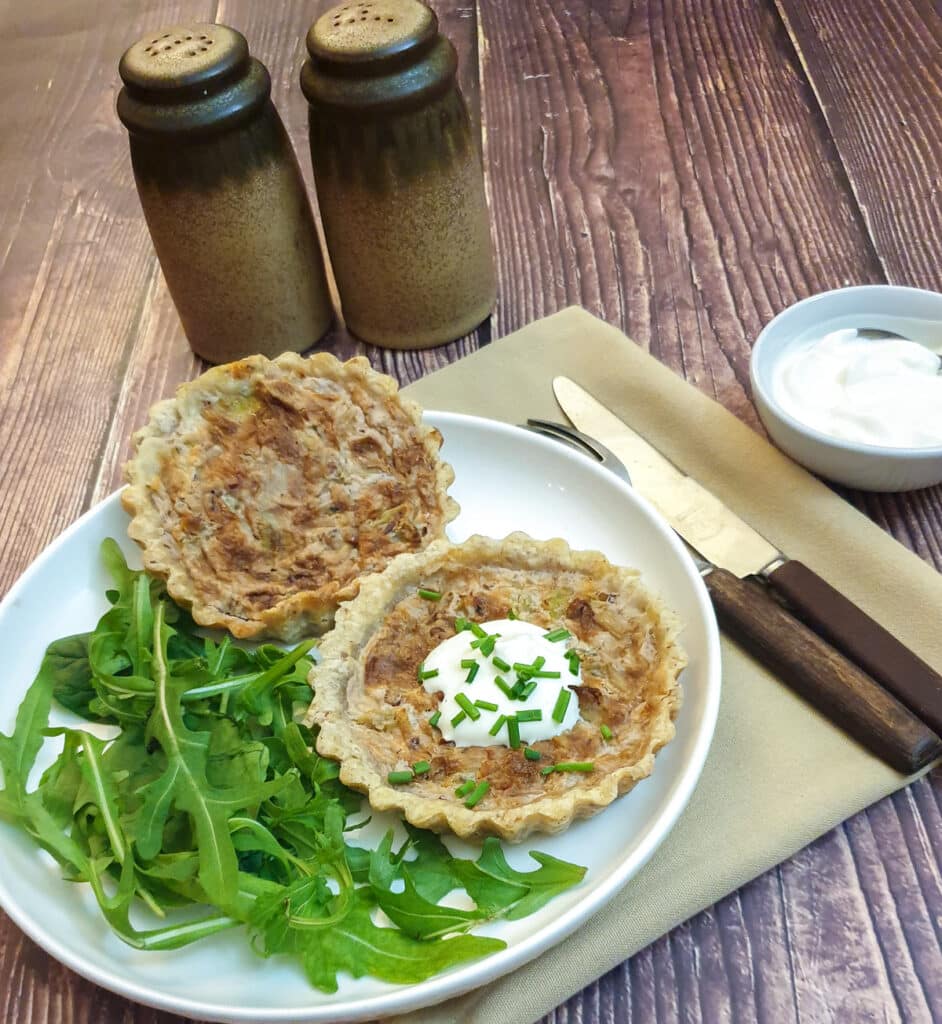 Two stilton and walnut tarts on a plate with rocket leaves.