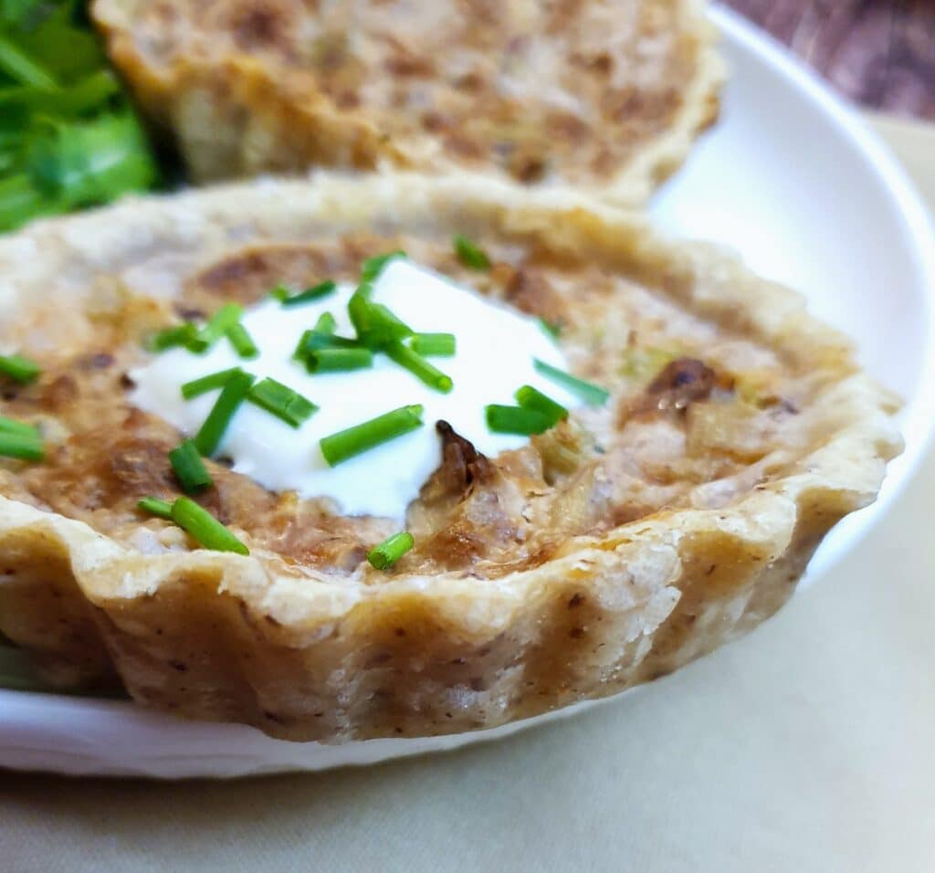 Closeup of a stilton and walnut tart garnished with creme fraiche and chopped chives.