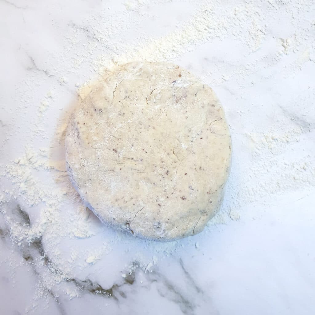 Walnut pastry formed into a flat disk on a floured work surface.