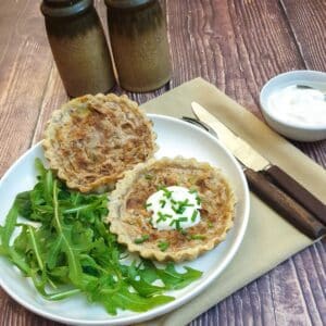 Two stilton and walnut tarts on a plate with rocket leaves.