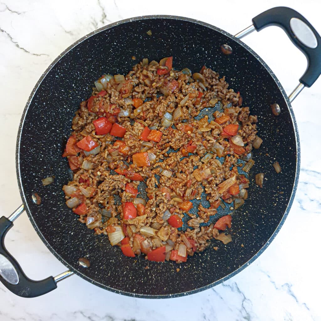 Lamb mince with onions, tomatoes and red peppers in a frying pan.