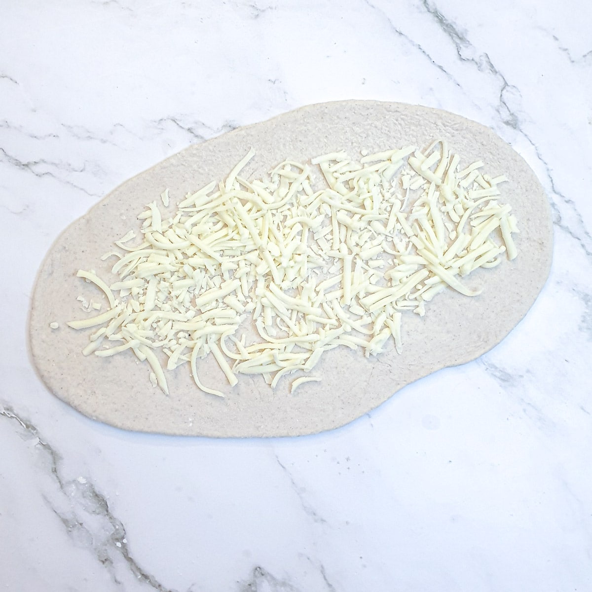 An oval shaped piece of dough topped with grate cheese.