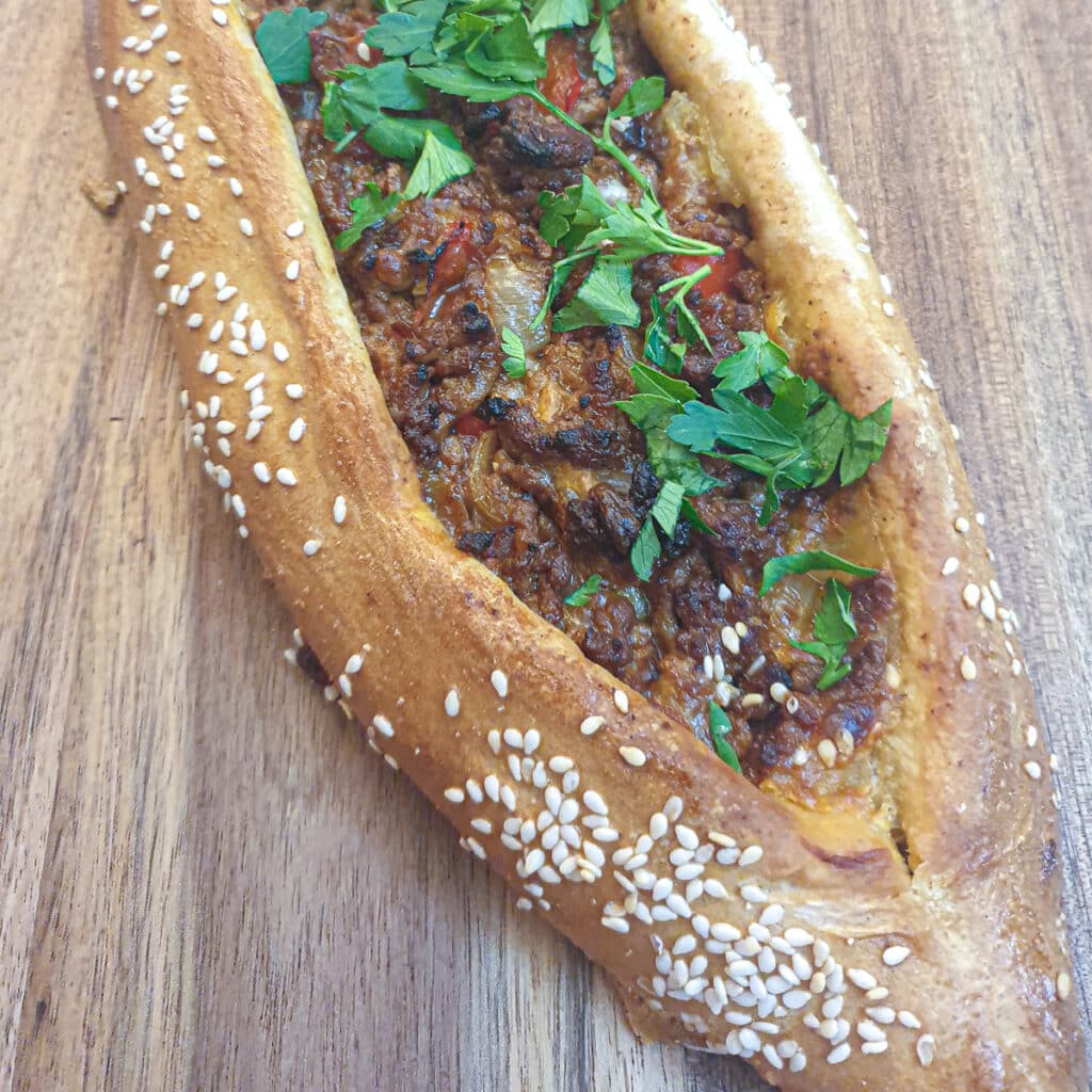 A close up of a baked lamb pide showing the sesame seeds on the crispy brown pastry.