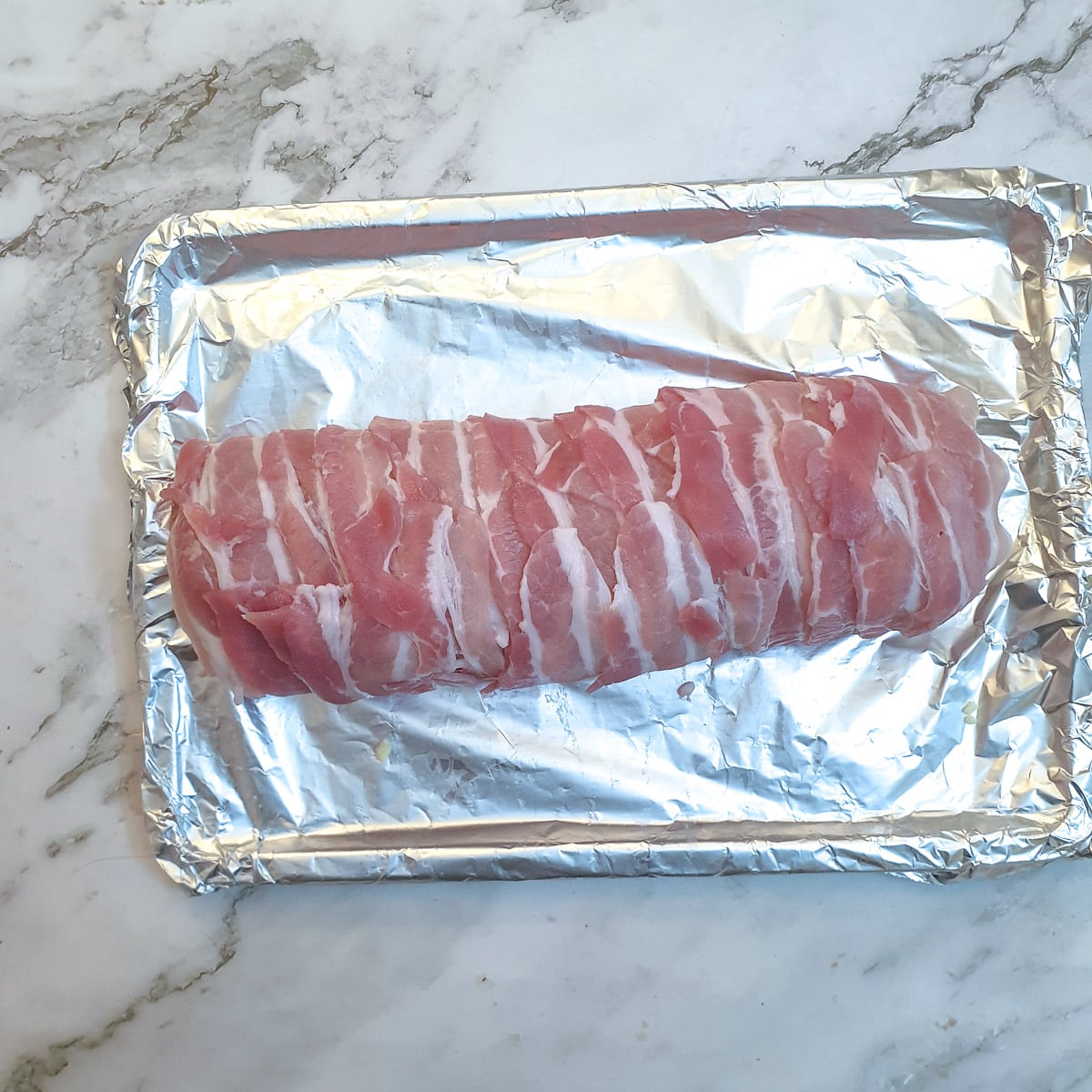 Raw chicken and bacon meatloaf on a baking tray.