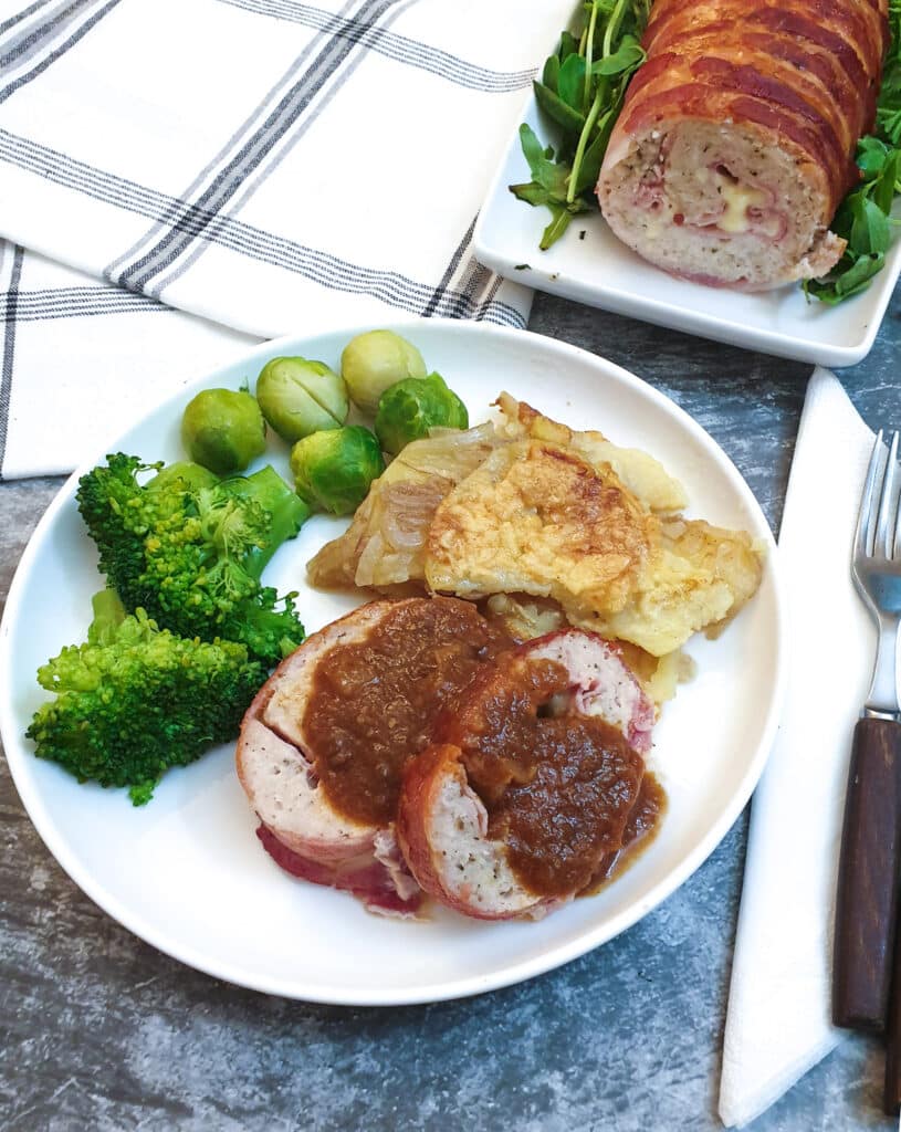 Slices of chicken and bacon meatloaf on a white plate with potatoes and vegetables.
