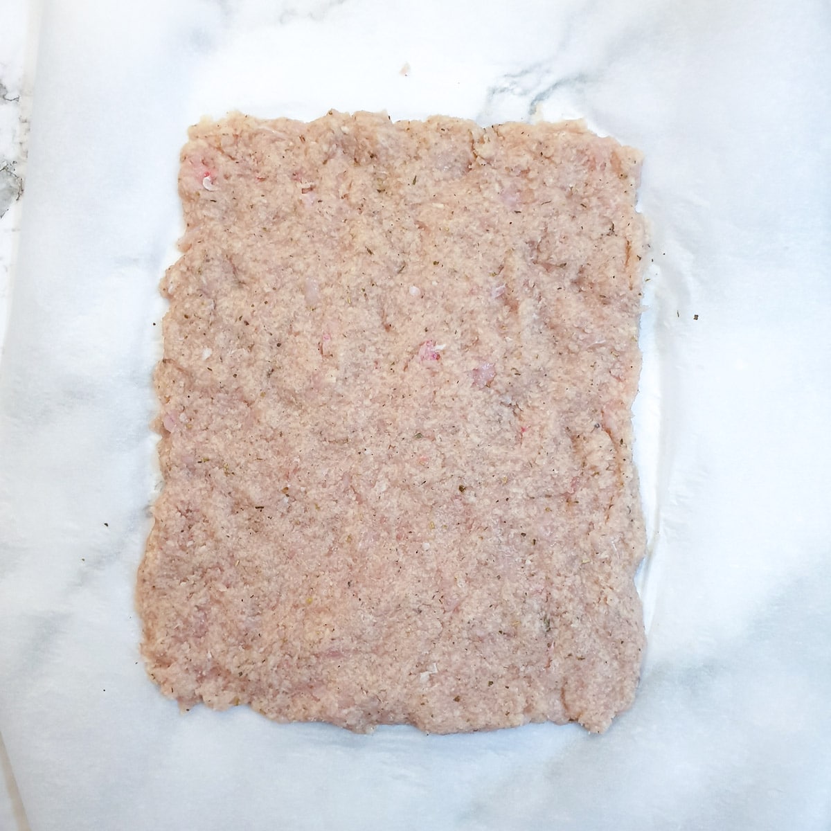 Minced chicken spread onto a sheet of parchment paper.