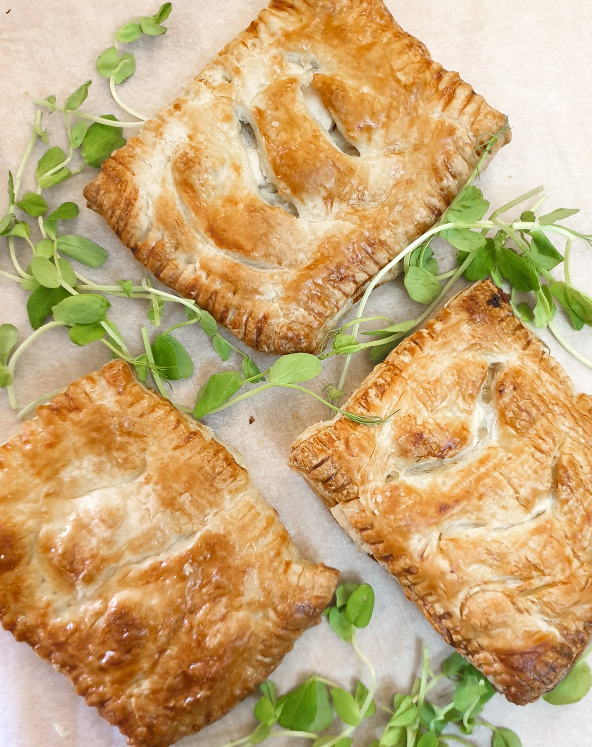 Three chicken and mushroom bakes on a tray, garnished with green pea shoots.