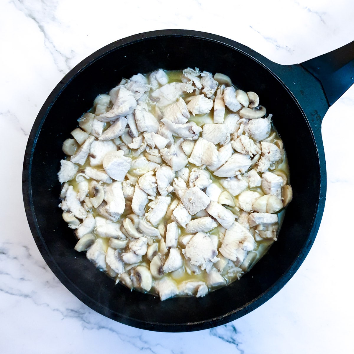 Mushrooms added to the chicken in a pan.