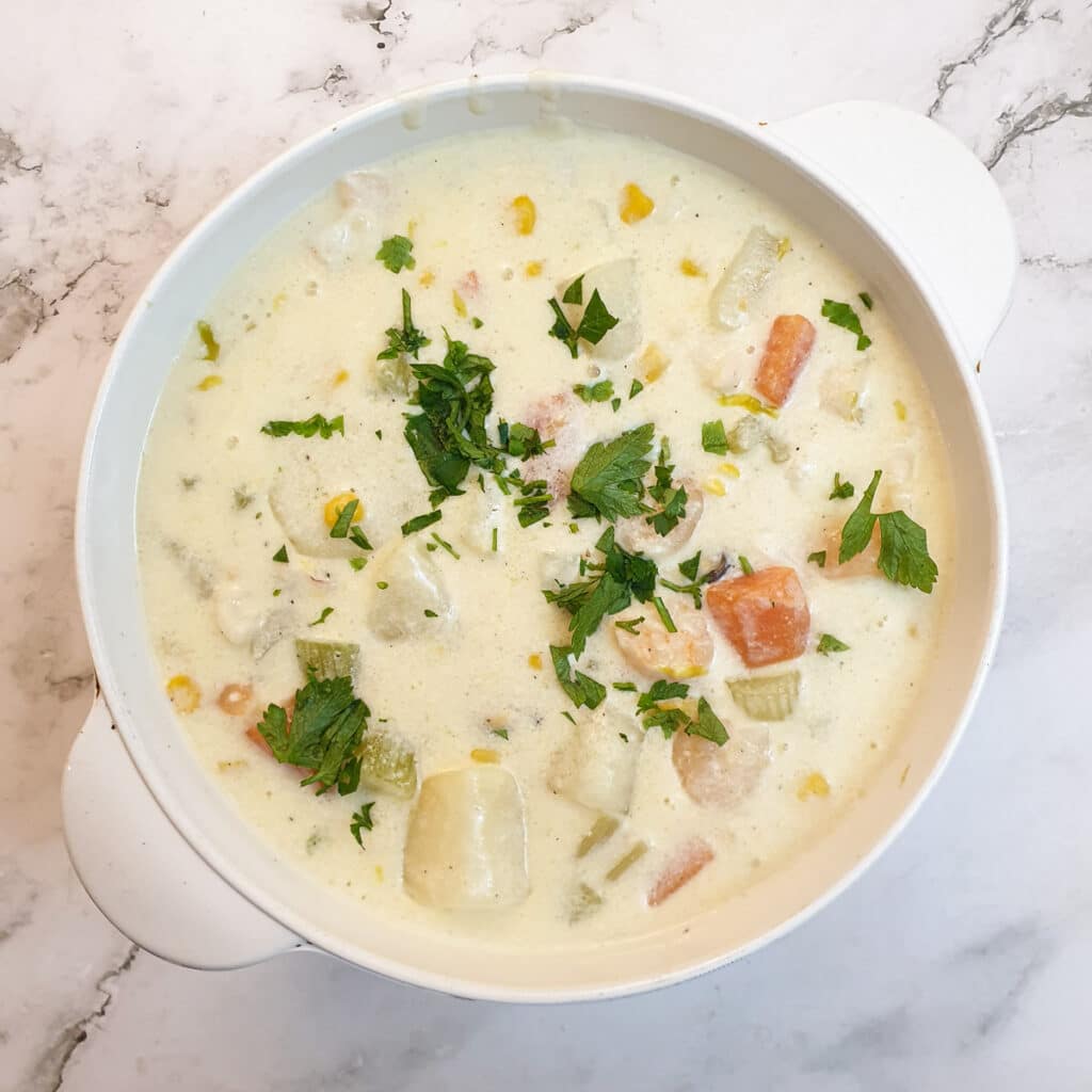 A white serving dish filled with seafood chowder and garnished with parsley.