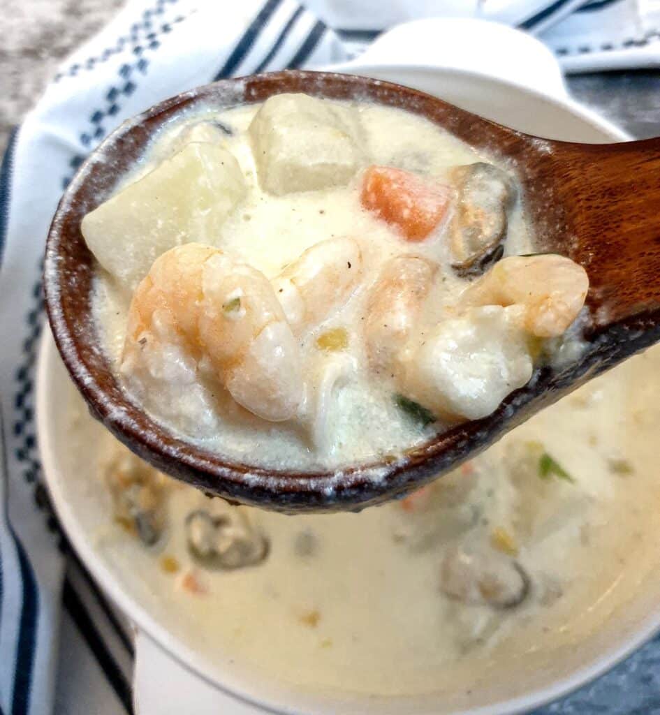 A wooden serving spoon filled with seafood chowder.