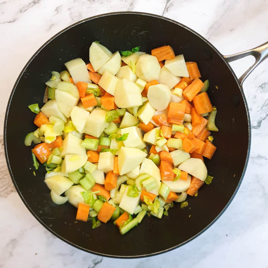 Potatoes, celery and carrots being cooked in butter.