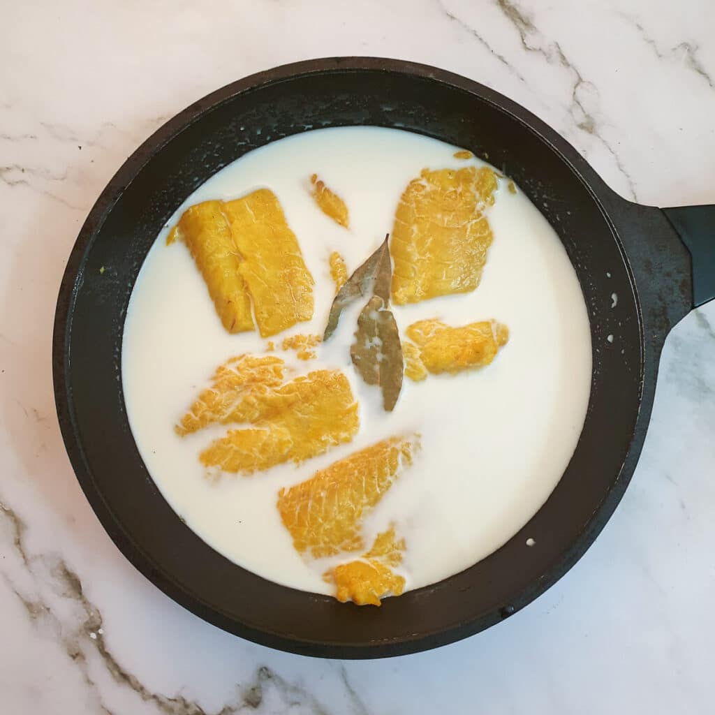 Smoked haddock poaching in a frying pan with milk.
