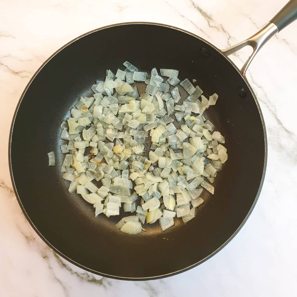 Chopped onions frying in oil in a frying pan.