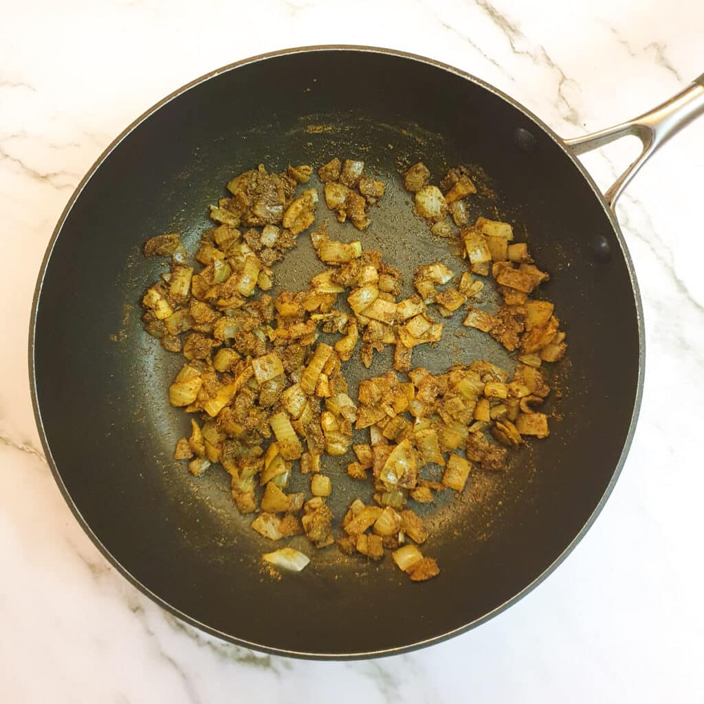 Curry spices mixed with onions in a frying pan.