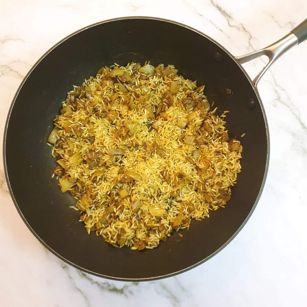 Rice added to the spice and onion mix in a frying pan.