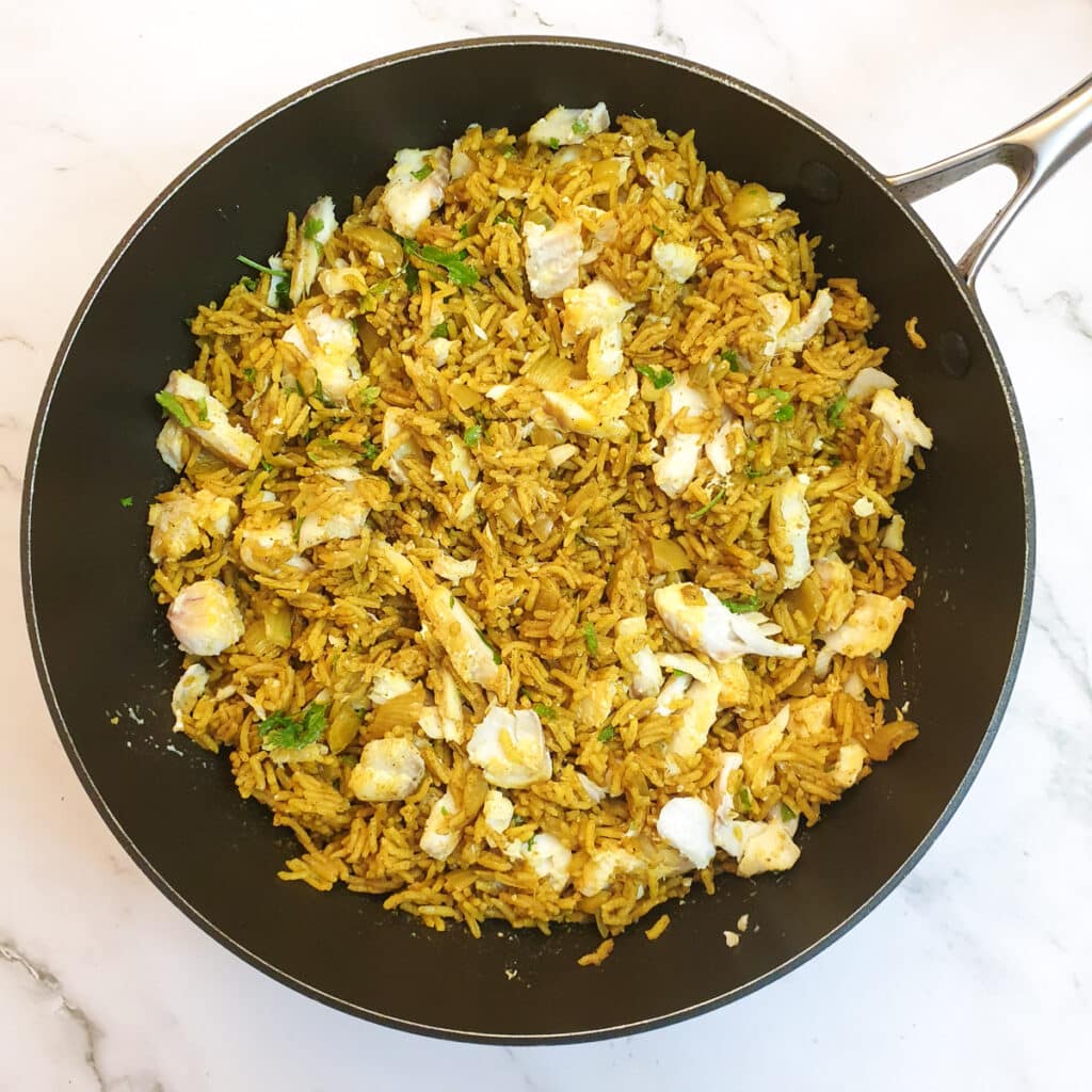 Flaked haddock mixed with rice in a frying pan.