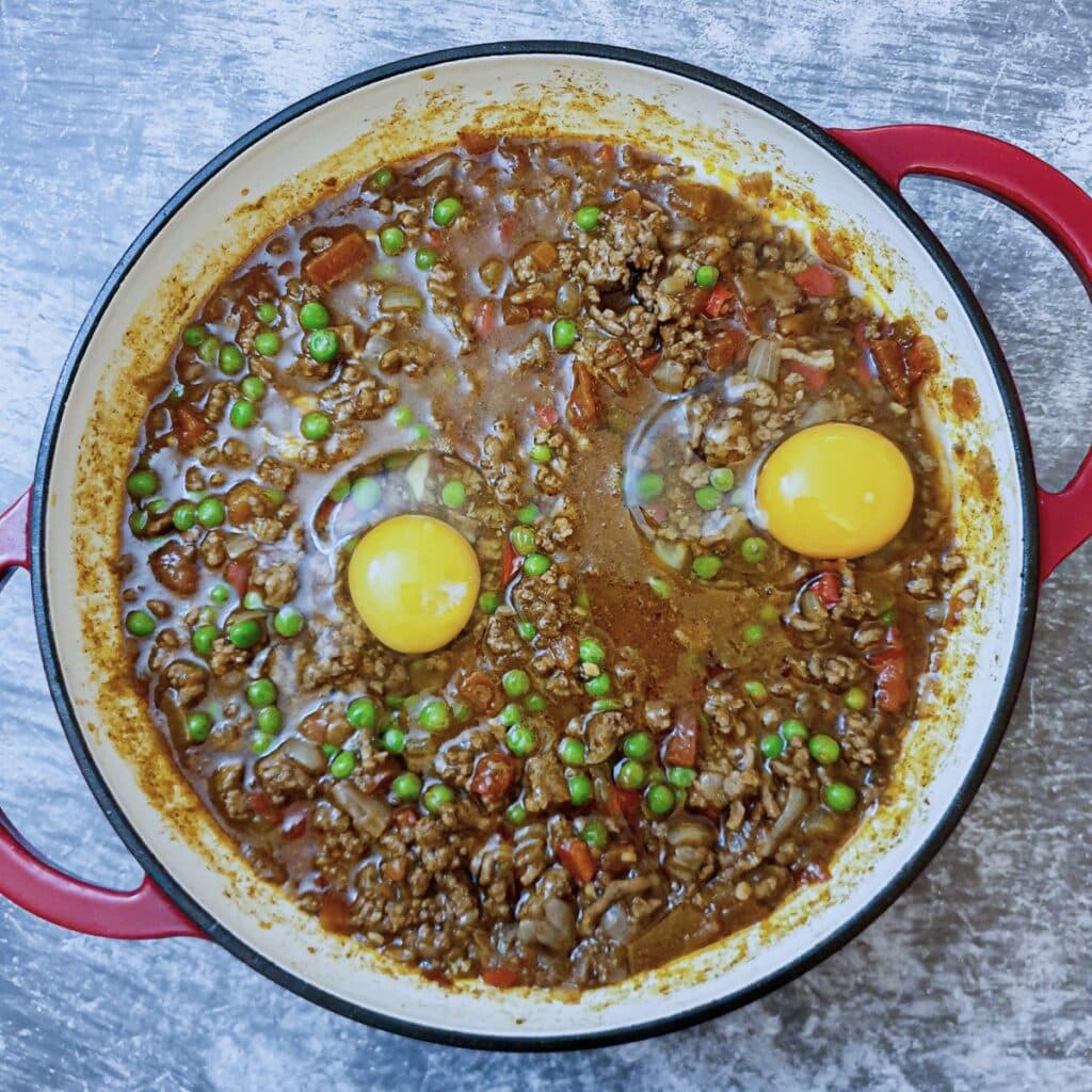 2 raw eggs on top of a pan of lamb keema.