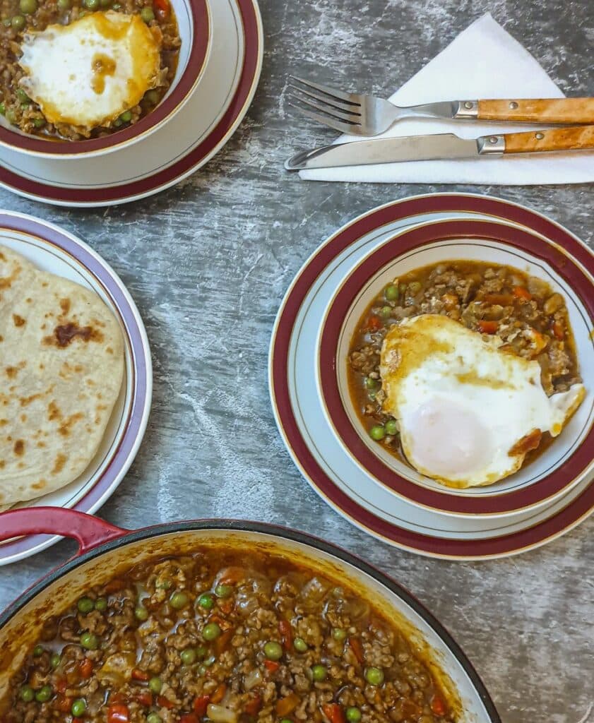 Lamb keema topped with egg in a dish on the table.