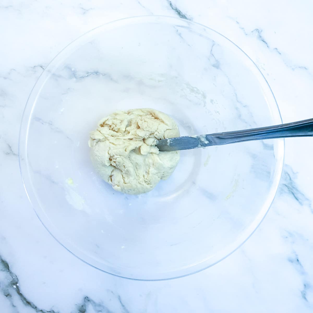 Flatbread dough being mixed with a flat-bladed knife in a mixing bowl.