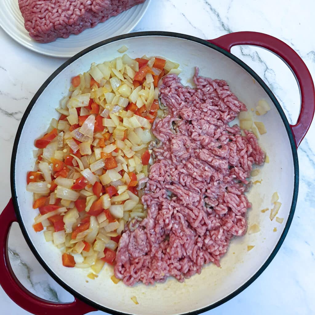 Red pepper and onions on one side of a pan with mince being browned on the other side.