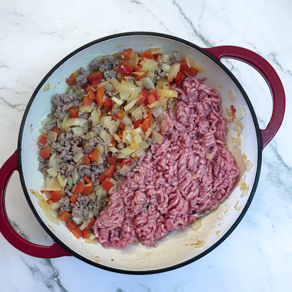 More mince being browned in a pan with onions and red peppers.