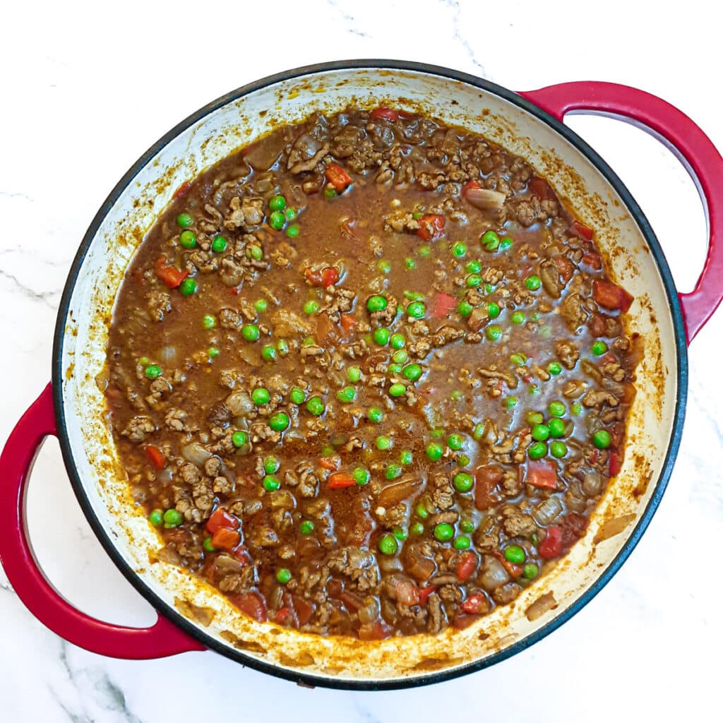 Peas added to a pan of lamb keema.