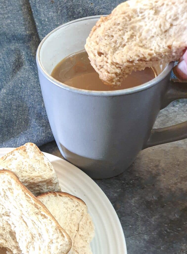 A dried rusk being dunked into a cup of coffee.