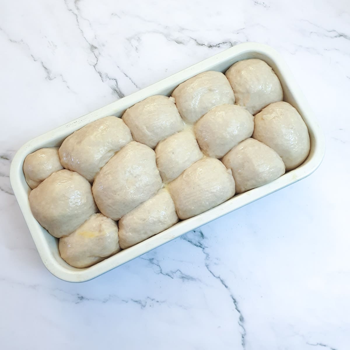 Balls of dough in a baking tin, after rising and doubling in size.