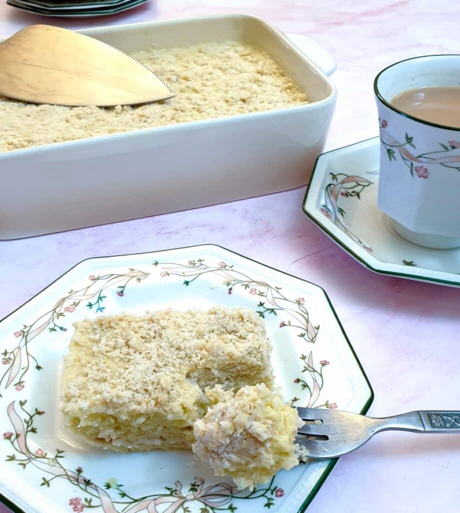 A slice of pineapple fridge tart on a plate next to a cup of tea.