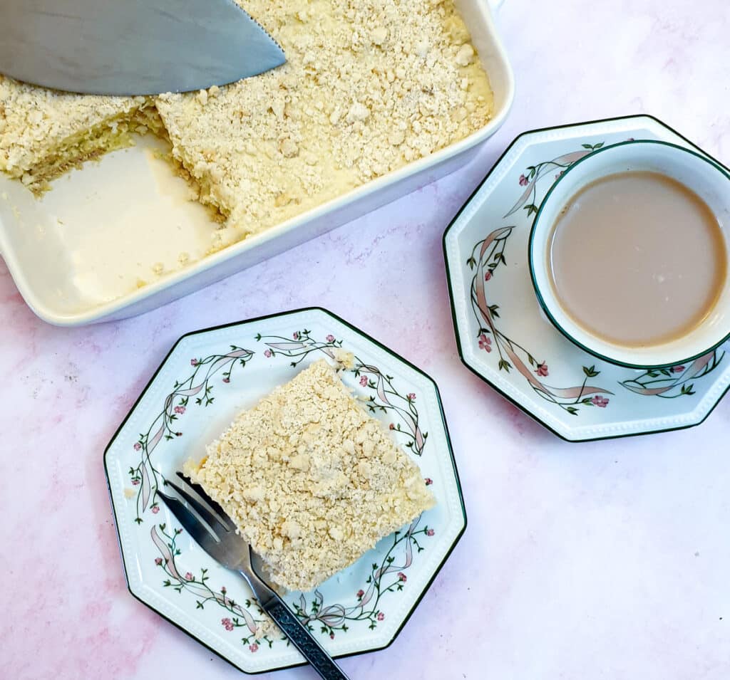 A slice of pineapple fridge cake on a plate next to a cup of tea.