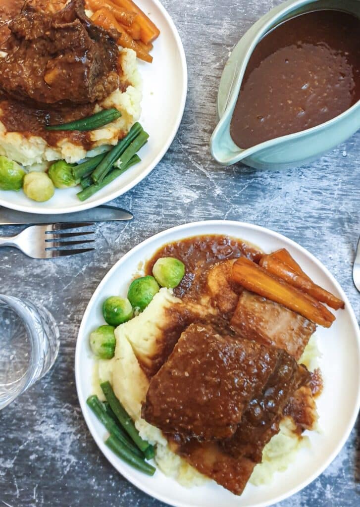 Overhead shot of 2 plates of beef spare ribs on a table with a jug of monkey gland sauce.