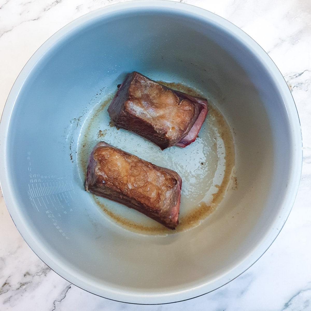 2 large beef short ribs being browned in the inner pot of a Ninja multi-cooker.