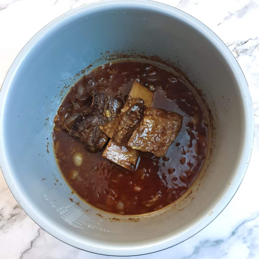 Cooked beef short rib in a Ninja multi-cooker showing how the meat has pulled back from the bone.