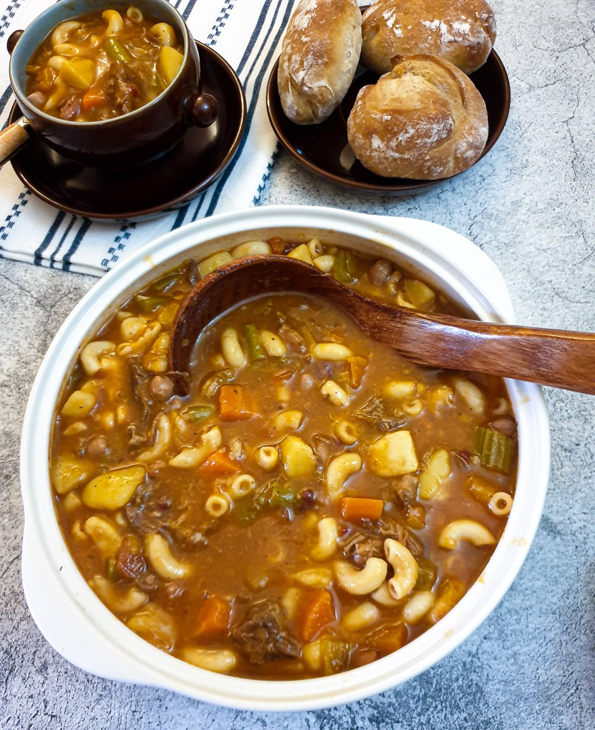 A serving bowl filled with beef minestrone soup with a wooden serving spoon.